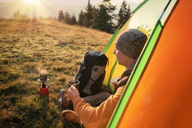 Man with cup of hot drink in camping tent outdoors