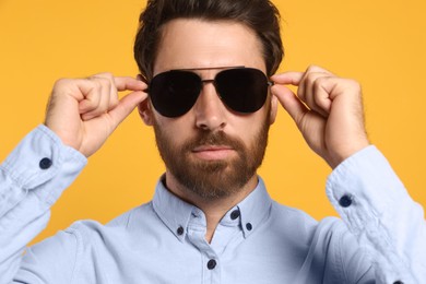 Portrait of bearded man with stylish sunglasses on orange background, closeup