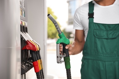 Worker with fuel pump nozzle at modern gas station, closeup