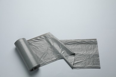 Photo of Roll of grey garbage bags on light background, top view