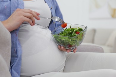 Photo of Pregnant woman with salad on sofa at home, closeup. Healthy diet