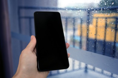 Photo of Woman holding smartphone with blank screen near window, closeup