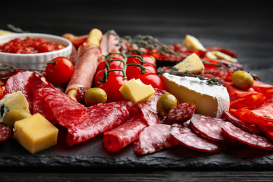 Photo of Tasty salami with other delicacies served on black table, closeup