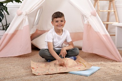 Photo of Cute little boy with treasure map near toy wigwam at home