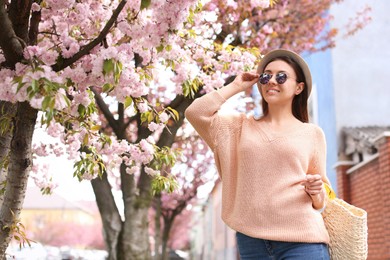 Photo of Happy stylish young woman near blossoming sakura tree outdoors. Spring look