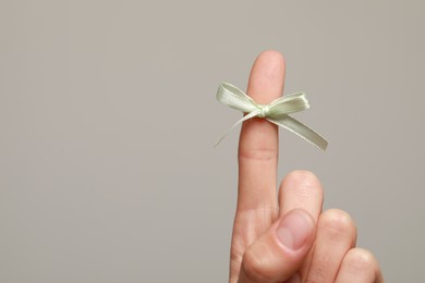 Photo of Woman showing index finger with tied bow as reminder on grey background, closeup. Space for text