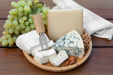 Different types of delicious cheeses, nuts and grapes on wooden table