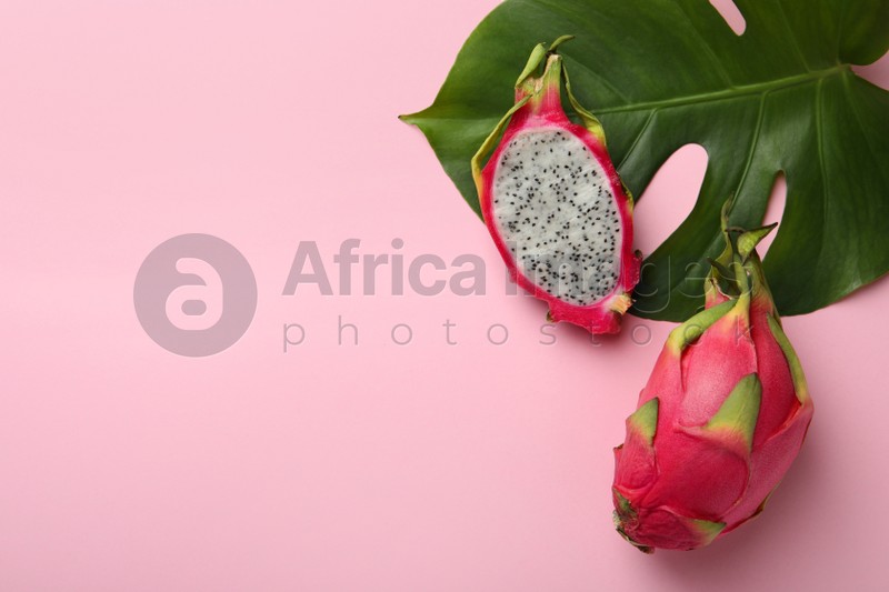 Delicious cut and whole white pitahaya fruits with green leaf on light pink background, flat lay. Space for text