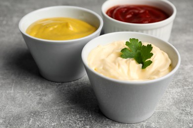 Bowls with mustard, ketchup and mayonnaise on light grey table, closeup