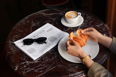 Woman breaking tasty croissant at black table, closeup
