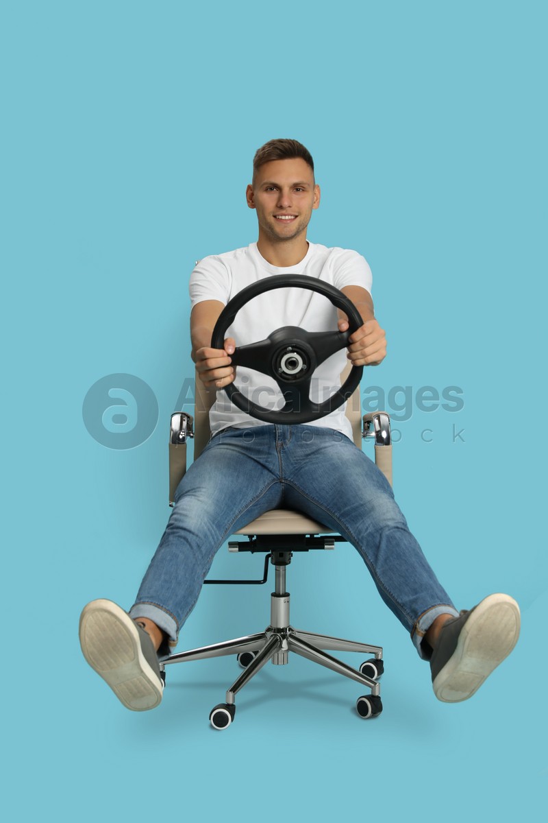 Happy man on chair with steering wheel against light blue background