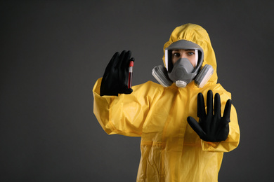 Woman in chemical protective suit holding test tube of blood sample on grey background. Virus research