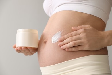 Young pregnant woman with cosmetic product on grey background, closeup