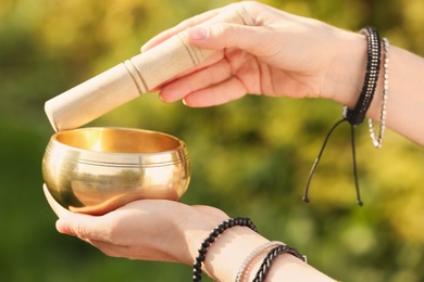 Woman using singing bowl in sound healing therapy outdoors, closeup
