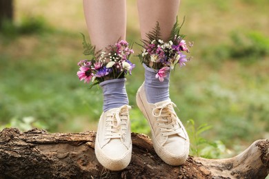 Woman standing on log with flowers in socks outdoors, closeup