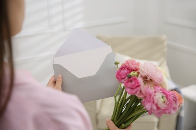 Woman holding envelope with blank greeting card and bouquet of ranunculus at home, closeup