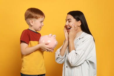 Mother and her son with ceramic piggy bank on orange background