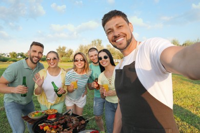Happy friends with drinks taking selfie at barbecue party in park