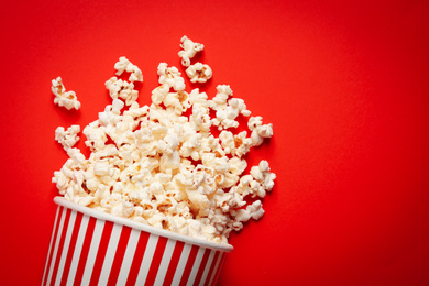 Overturned paper cup with delicious popcorn on red background, top view