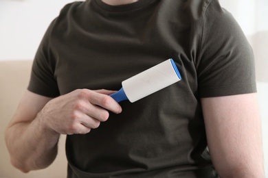 Photo of Man cleaning grey t-shirt with lint roller on light background, closeup