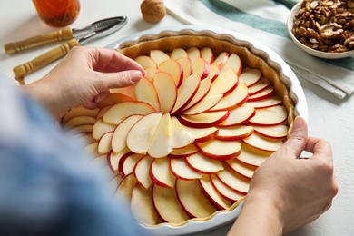 Woman putting apple slices into baking dish with dough to make traditional English pie at white table, closeup