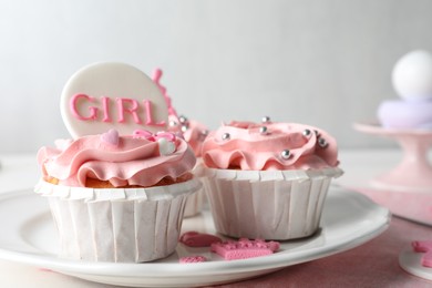 Photo of Delicious cupcakes with pink cream and toppers for baby shower on plate, closeup