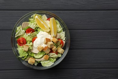 Bowl of delicious salad with Chinese cabbage, tomatoes and bread croutons on black wooden table, top view. Space for text