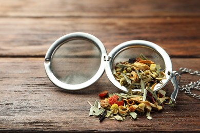 Photo of Snap infuser with dried herbal tea leaves on wooden table, closeup