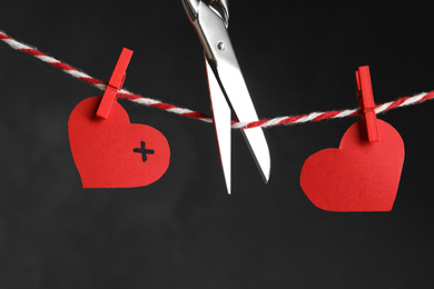 Red paper hearts on rope and scissors against black background. Composition symbolizing problems in relationship