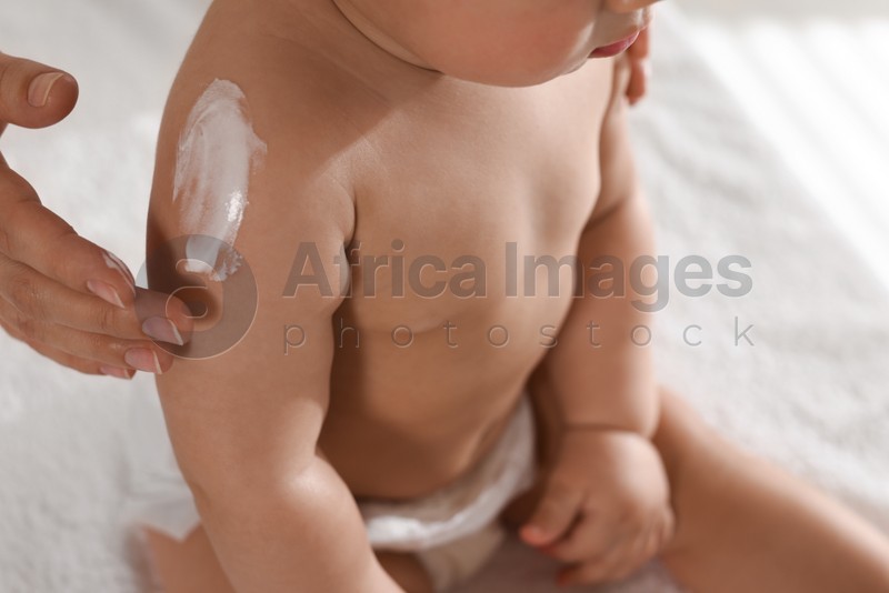 Photo of Mother applying body cream on her little baby at home, closeup