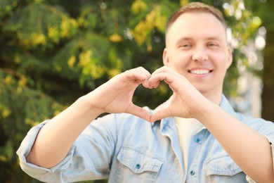 Photo of Man making heart with hands outdoors on sunny day, closeup