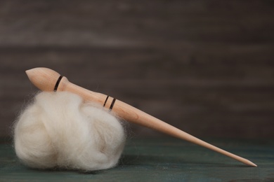 Photo of Soft white wool and spindle on blue wooden table. Space for text