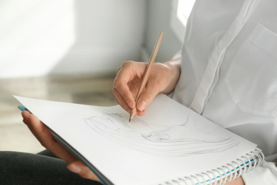 Woman drawing girl's portrait with pencil in notepad, closeup