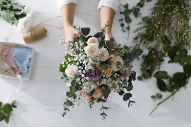Florist holding beautiful wedding bouquet at white table, top view