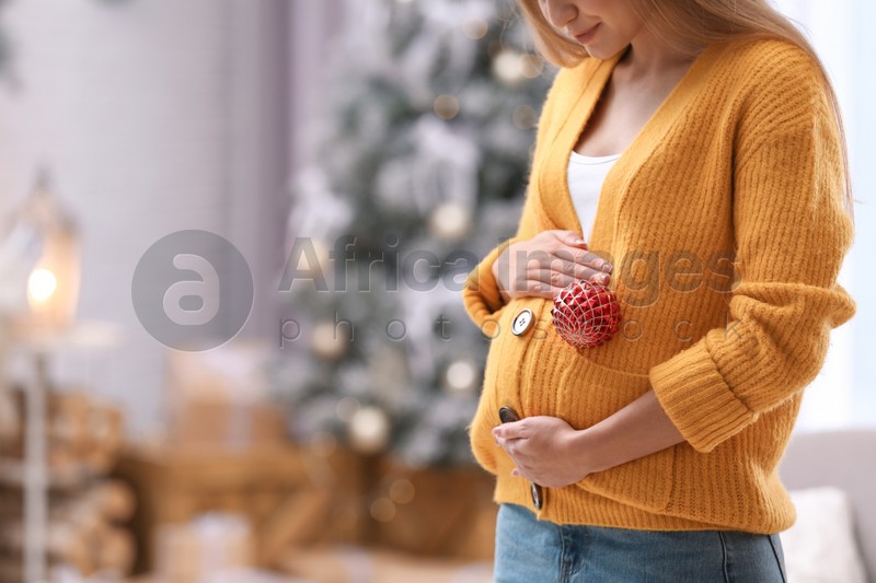 Young pregnant woman with Christmas decoration at home, closeup. Space for text
