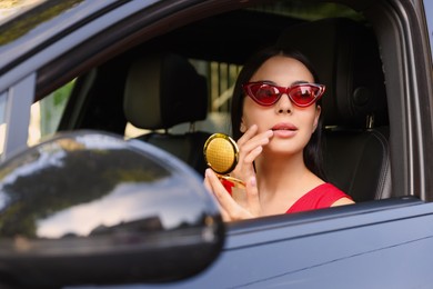Photo of Beautiful young woman with cosmetic pocket mirror in car