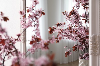 Blossoming tree twigs in vase near mirror indoors, closeup