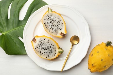 Photo of Delicious dragon fruits (pitahaya) and tropical leaf on white wooden table, flat lay