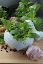 Photo of Mortar with different fresh herbs near garlic, horseradish roots and black peppercorns on wooden table, closeup