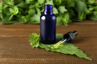 Glass bottle of nettle oil with dropper and fresh leaf on wooden table