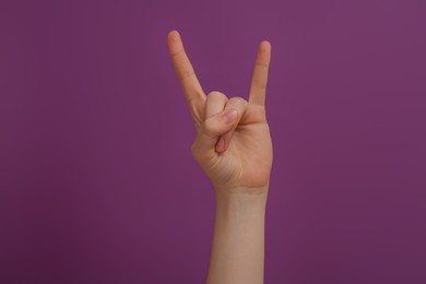 Woman showing gesture of horns on purple background, closeup