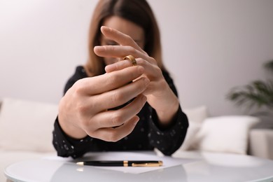 Woman taking off wedding ring at table indoors, focus on hands. Divorce concept