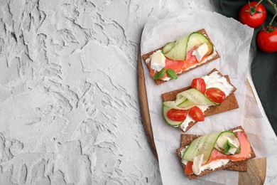 Tasty rye crispbreads with salmon, cream cheese and vegetables on grey textured table, flat lay. Space for text