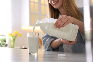 Young woman pouring milk from gallon bottle into glass at white marble table in kitchen, closeup