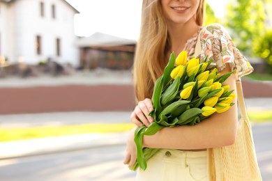 Photo of Teenage girl with bouquet of yellow tulips on city street, closeup. Space for text