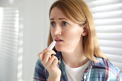 Photo of Upset woman with herpes applying lip balm indoors