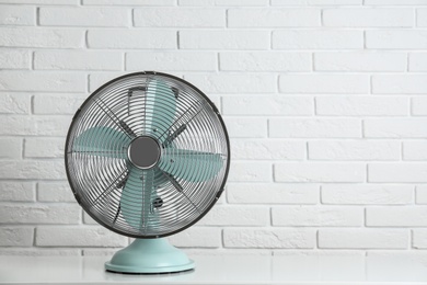 Electric fan on table near white brick wall, space for text. Summer heat