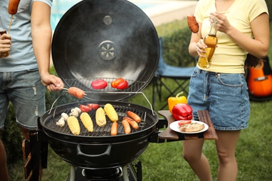 People with sausages near barbecue grill outdoors, closeup