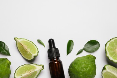 Glass bottle of bergamot essential oil and fresh fruits on white background, flat lay. Space for text
