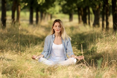 Young woman meditating in forest on sunny day